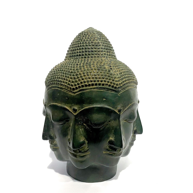 May include: A dark green Buddha head sculpture with four faces and a detailed, textured topknot. The sculpture has a weathered appearance, suggesting age or a vintage style. The faces are serene, with closed eyes and subtle features.