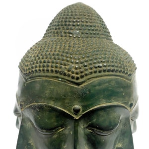 May include: A close-up of a weathered, green-toned Buddha head statue. The statue features closed eyes, a serene expression, and a detailed, textured hairstyle. The head is set against a plain white background, highlighting the sculpture's intricate details.