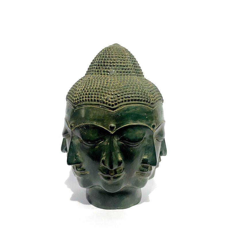 May include: A dark green, multi-faced Buddha head sculpture. The sculpture features four visible faces and a textured, rounded top. The faces have serene expressions and closed eyes. The sculpture is set against a white background.