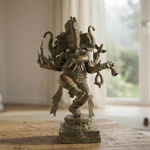 Op de afbeelding: Bronzen beeld van de hindoe&iuml;stische godheid Ganesha, afgebeeld met een olifantenkop en meerdere armen, staand op een vierkante basis. Het beeld staat op een houten tafel, met een yogamat en opgevouwen handdoeken op de achtergrond.