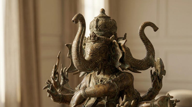 Op de afbeelding: Bronzen beeld van Ganesha, de hindoe&iuml;stische god van wijsheid en voorspoed. De sculptuur heeft een olifantenkop met meerdere armen, die verschillende objecten vasthouden. Het beeld is ingewikkeld gedetailleerd en heeft een verweerde uitstraling.