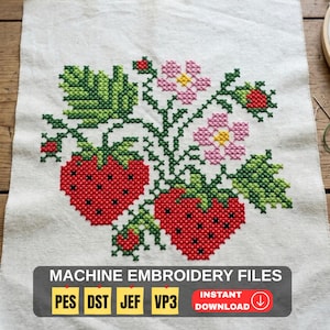 Op de afbeelding: Kruissteekborduurwerk op stof met twee rode aardbeien, groene bladeren en roze bloemen. Het ontwerp bevat de tekst "MACHINE EMBROIDERY FILES" en afkortingen van bestandstypen.