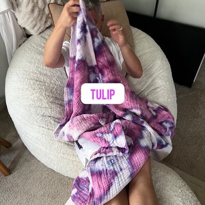 May include: A person sitting in a white beanbag chair, holding a pink and purple tie-dye blanket with the word "TULIP" printed on it.
