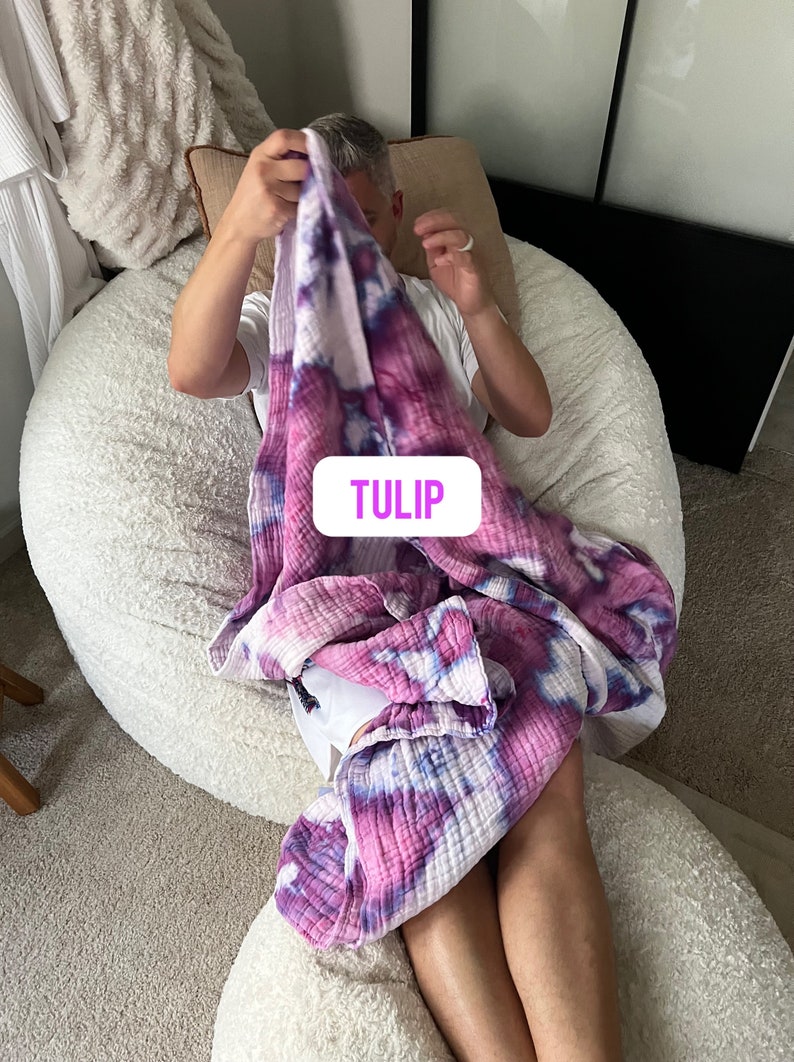 May include: A person sitting in a white beanbag chair, holding a pink and purple tie-dye blanket with the word "TULIP" printed on it.