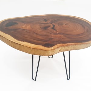 May include: A wooden coffee table with a natural wood top and a unique, irregular shape. The table has four black hairpin legs.