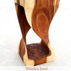 May include: A wooden stool with an hourglass shape, crafted from light and dark brown wood. The stool has a polished finish. Dimensions: 60 cm (H) x 30 cm (W). The text "Wooden Stool" is displayed. A decorative furniture item.