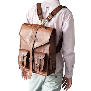 Peut inclure: Un sac à dos en cuir marron avec plusieurs poches et des bretelles réglables. Le sac à dos a une fermeture à rabat et des détails de boucles. Le sac est porté sur les épaules.