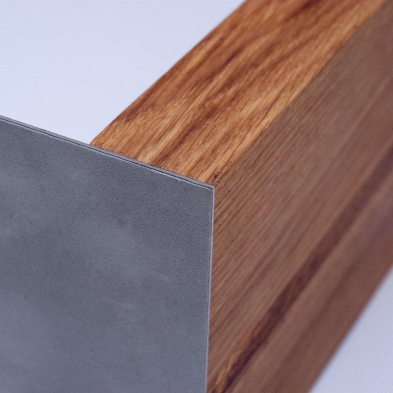 May include: Close-up of a wooden beam with a metal corner protector. The wood grain is visible, showing a warm brown color. The metal corner is a cool gray, providing a contrast to the wood. The design is modern and minimalist.