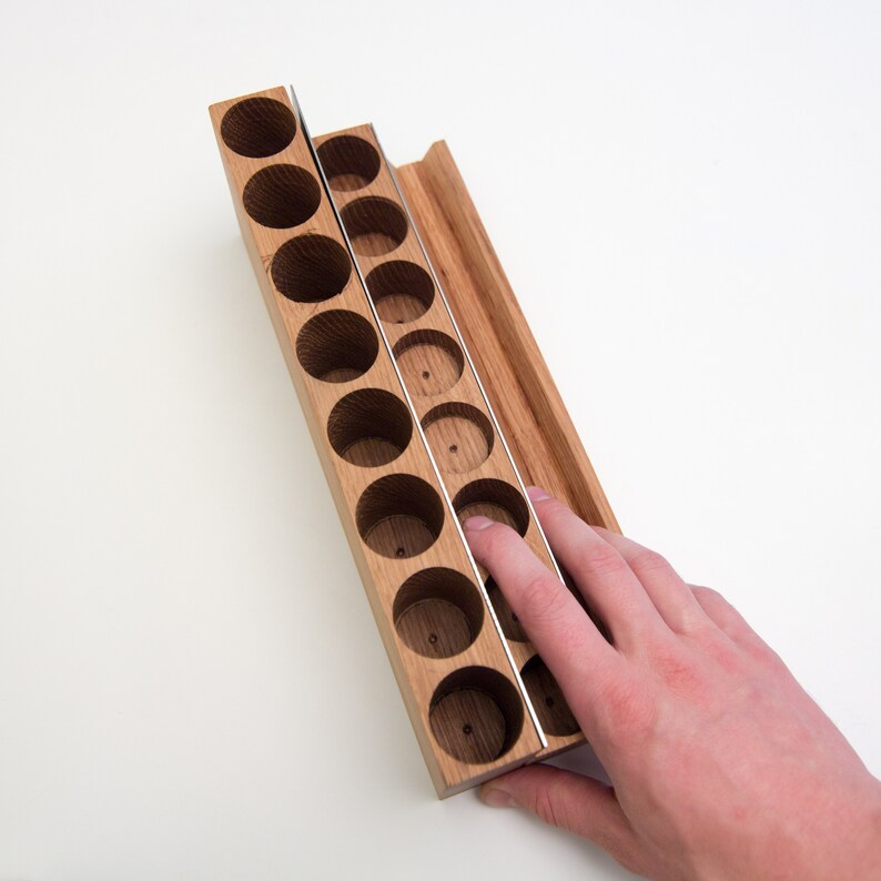 Puede incluir: Un organizador de madera con 18 compartimentos para guardar objetos peque&ntilde;os. El organizador est&aacute; hecho de madera marr&oacute;n claro y tiene un divisor de metal. El organizador est&aacute; abierto y una mano est&aacute; llegando a los compartimentos.