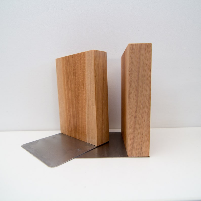 May include: Wooden bookends with a natural wood grain finish. The bookends are rectangular and sit on a brushed metal base. The design is minimalist and modern, suitable for home or office decor.