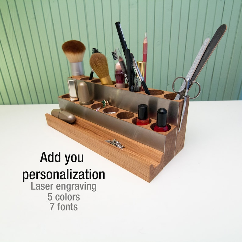Puede incluir: Organizador de madera con inserciones met&aacute;licas para guardar pinceles de maquillaje, esmalte de u&ntilde;as y otros art&iacute;culos de belleza. El organizador tiene dos niveles y est&aacute; hecho de madera natural. El texto "Add you personalization Laser engraving 5 colors 7 fonts" est&aacute; impreso debajo del organizador.