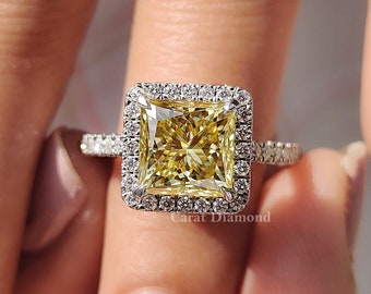 May include: A square-shaped yellow diamond engagement ring with a halo setting. The ring is set in white gold and has a pave band.