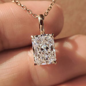 May include: A gold necklace featuring a rectangular, radiant-cut diamond pendant. The diamond is set in a gold bezel and hangs from a delicate gold chain. The pendant is held up by a gold bail.