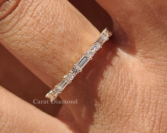 May include: A gold band ring with a row of small, rectangular diamonds set in a pave setting. The ring is on a person's finger.