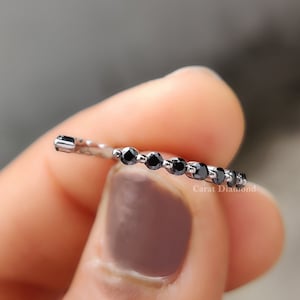 May include: A delicate silver band set with a row of small, round black diamonds. The diamonds are evenly spaced along the band.