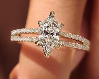 Pode incluir: Um anel de noivado dourado com um diamante central em corte marquise. A banda apresenta um design de haste dividida com diamantes cravejados em pavé. O anel é apresentado sobre um fundo desfocado.