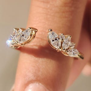 Peut inclure: Une bague dorée au design ouvert. La bague est ornée de plusieurs diamants taille marquise, disposés en motif floral ou en forme de feuille. Les diamants sont sertis à griffes, créant un aspect étincelant et élégant. C'est un bijou.