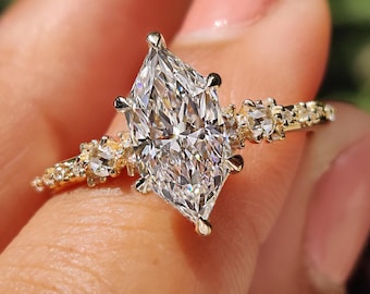 Puede incluir: Un anillo de oro con un gran diamante de talla marquesa como pieza central. La banda también está adornada con diamantes más pequeños, creando un efecto brillante. El anillo está sostenido por un dedo.