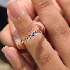 Puede incluir: Un anillo de banda de oro con tres diamantes talla baguette engastados en fila. El anillo está en un dedo.