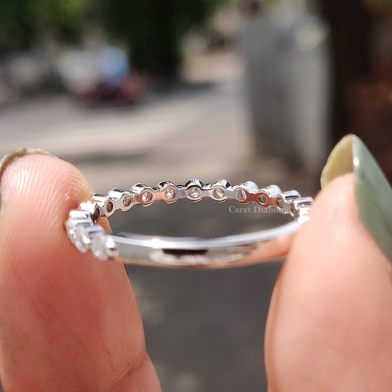 K&ouml;nnte beinhalten: Ein silberner Bandring mit einer Reihe kleiner runder Diamanten, die in einer Pav&eacute;-Fassung gefasst sind. Der Ring wird von der Seite gezeigt, wobei die Diamanten zum Betrachter zeigen.