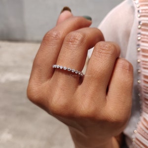 K&ouml;nnte beinhalten: Ein zarter Ewigkeitsring mit einer Reihe kleiner, runder, klarer Diamanten, die in eine silberne Band gefasst sind.