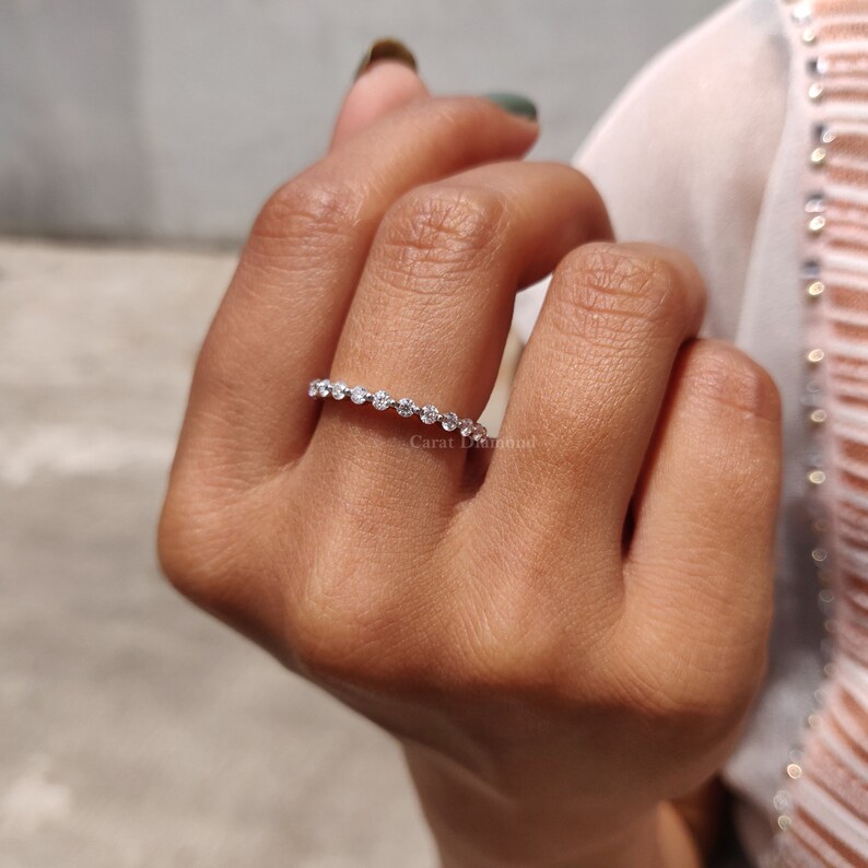 K&ouml;nnte beinhalten: Ein zarter Ewigkeitsring mit einer Reihe kleiner, runder, klarer Diamanten, die in eine silberne Band gefasst sind.