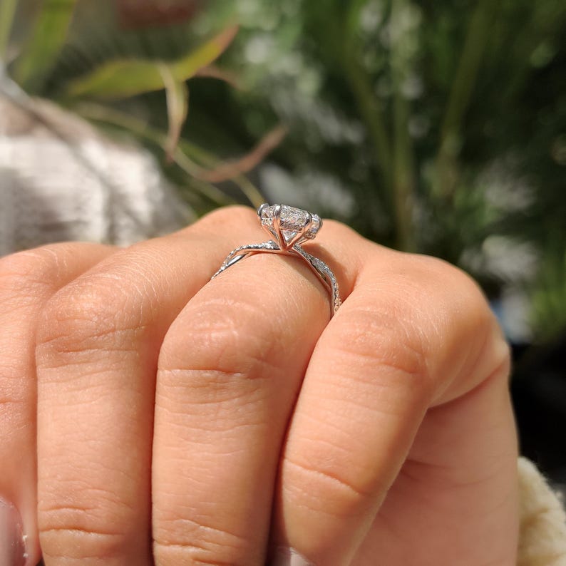 May include: A diamond engagement ring with a twisted band. The ring has a large, clear, round-cut diamond in a prong setting. The band is made of a shiny, silver-coloured metal. The ring is held by a hand.