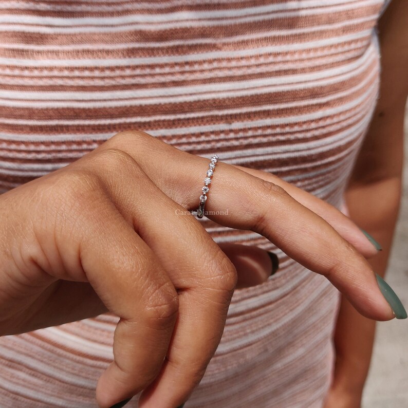 K&ouml;nnte beinhalten: Ein zarter Silberring mit einer Reihe kleiner, klarer Diamanten. Der Ring befindet sich an einem Finger.