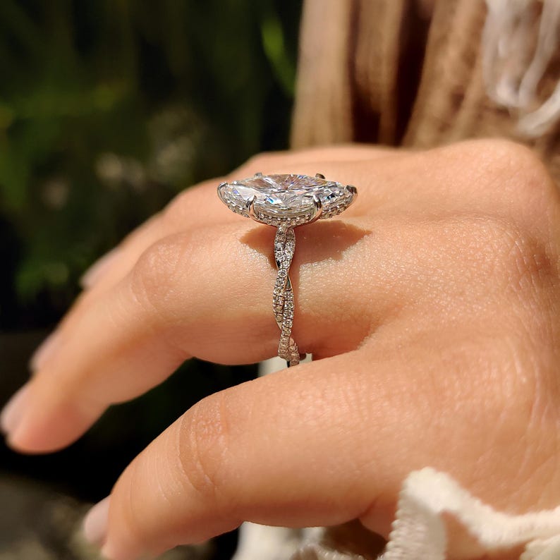 May include: A diamond ring with a large, oval-cut central stone. The ring has a halo of smaller diamonds and a twisted band. The ring is set in a silver metal.