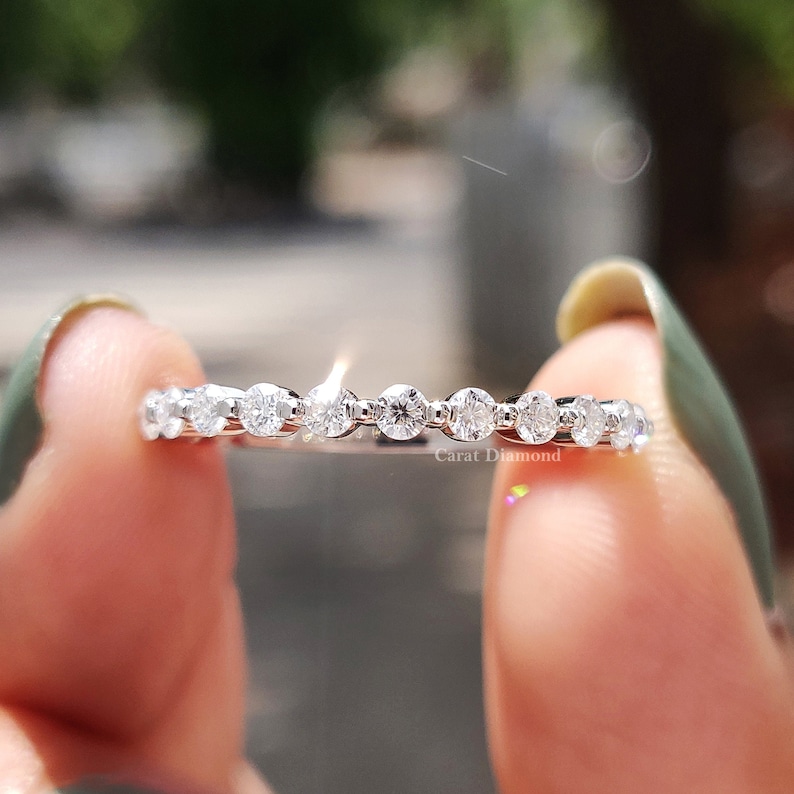 K&ouml;nnte beinhalten: Ein zartes Silberband mit einer Reihe kleiner, runder Diamanten, die in einem geschwungenen Muster gesetzt sind. Das Band wird an einem Finger gezeigt.