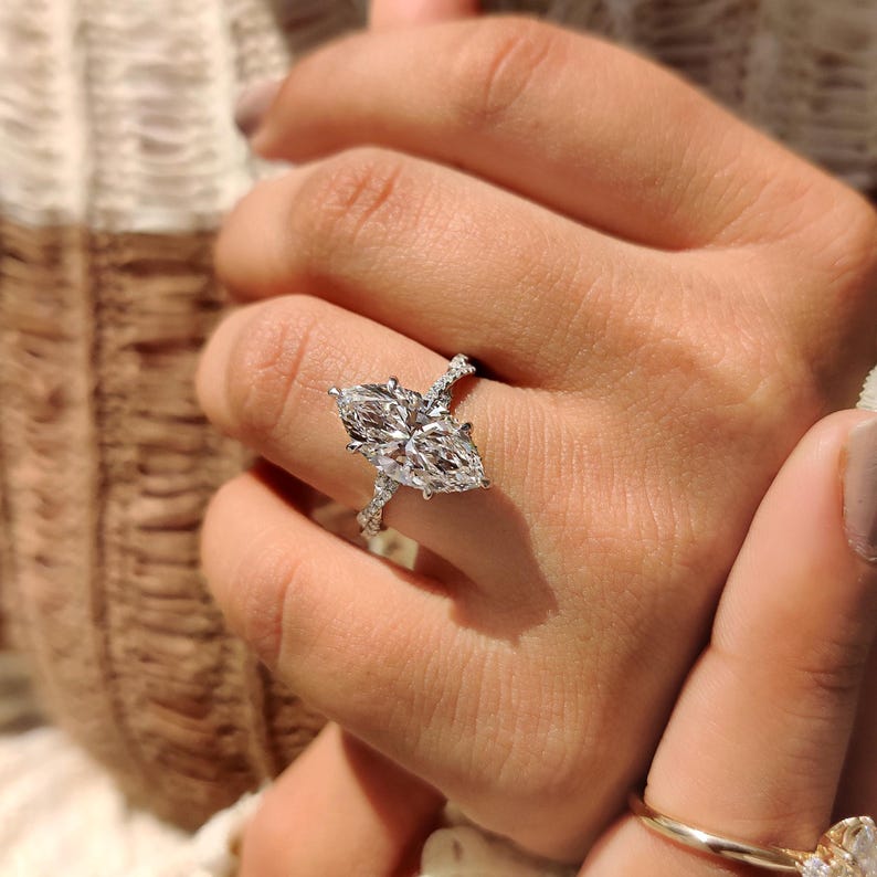 May include: A marquise-cut diamond ring with a twisted band. The ring features a large, clear, sparkling centre stone, set in a prong setting. The band is adorned with smaller accent diamonds, enhancing the ring's brilliance and sparkle.
