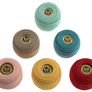Op de afbeelding: Een verzameling van zeven bollen haakgaren in verschillende kleuren, waaronder teal, bruin, roze, geel en rood. Elke bol heeft een rond label met een vlinderontwerp en de tekst "Crochet Yarn".