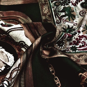 Può includere: Primo piano di un tessuto con un motivo paisley in tonalità di marrone, verde e bianco. Il tessuto è piegato e drappeggiato, creando un effetto testurizzato.