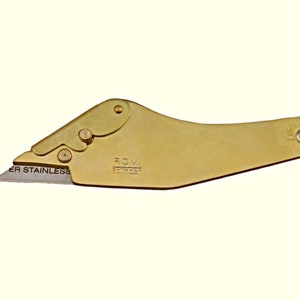 Könnte beinhalten: Ein goldfarbenes, taschenformatiges Universalmesser mit einer silbernen Klinge. Die Klinge ist mit "SUPER STAINLESS" beschriftet. Der Griff trägt die Gravuren "ROMI" und "SOLINGEN".