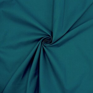 May include: A close-up of a teal fabric with a smooth texture. The fabric is folded and draped, creating soft folds and curves.
