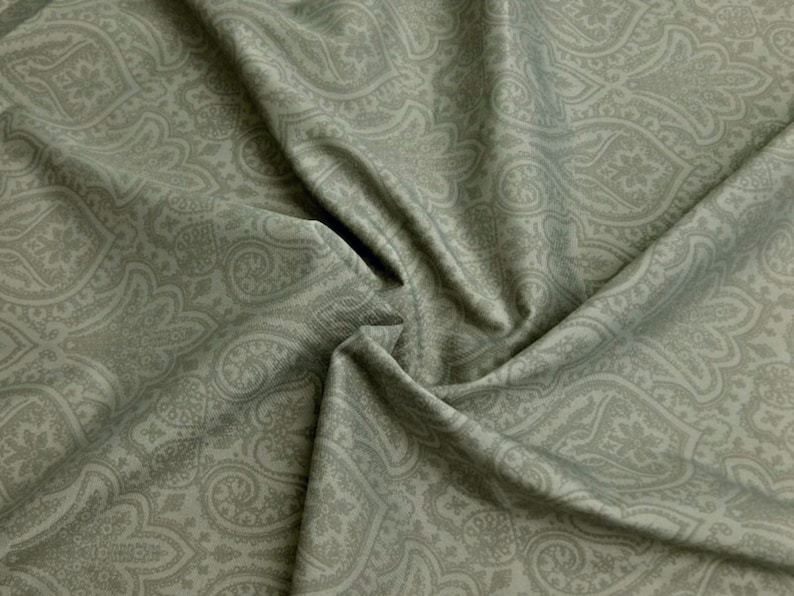 Może przedstawiać: Zbliżenie na zielony materiał z wzorem paisley. Materiał jest miękki i ma subtelny połysk.