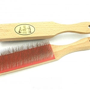 May include: Two wooden pet grooming brushes. One brush has a rectangular head with a red base and metal bristles. The other brush has a wooden head with an oval logo and a handle with a hole for hanging.
