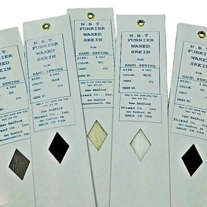 May include: Five white paper labels with black text and a diamond-shaped color swatch. The labels are for N.B.T. Furrier Waxed Skein thread for hand sewing. The labels list the size, color, and yardage of the thread. The colors are black, white, beige, and two shades of gray.