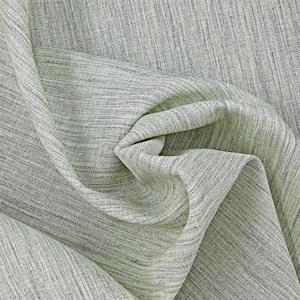 May include: A close-up of a light grey fabric with a subtle textured pattern. The fabric is folded and draped, showcasing its soft and drapey texture.