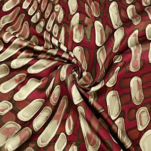Könnte beinhalten: Roter Satin-Stoff mit einem Muster aus beige und braunen abstrakten Formen.