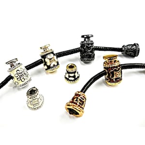 Peut inclure: Un assortiment de perles décoratives de différentes couleurs et motifs. Les perles sont attachées à des cordons noirs et présentent des accents dorés, argentés, noirs et blancs. Certaines perles ont des motifs floraux ou géométriques, d'autres sont de couleur unie.