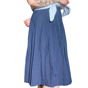 Puede incluir: Una camisa vaquera sin mangas atada a la cintura, combinada con una falda midi azul marino con lunares blancos. El conjunto es informal y elegante, adecuado para el día a día. La falda llega a media pantorrilla.