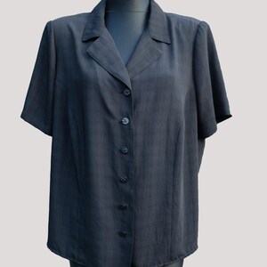 May include: A dark gray short-sleeved button-down shirt with a collared neckline. The shirt has a tailored fit and is displayed on a mannequin. The buttons are the same color as the shirt.