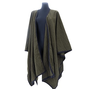 Puede incluir: Un poncho de punto verde con ribete negro. El poncho está drapeado sobre un maniquí.