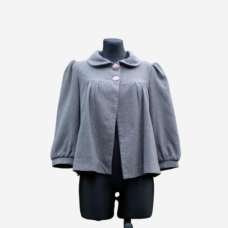 A gray coat with puffed sleeves and buttons is displayed on a mannequin.