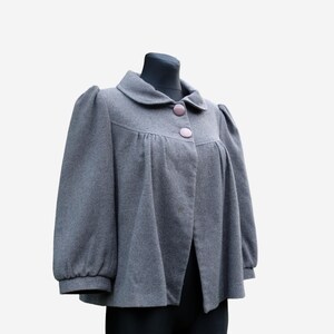 A gray wool coat with puffed sleeves and buttons is displayed on a mannequin.