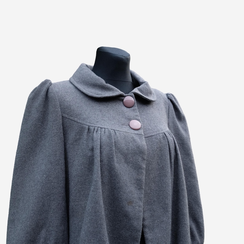 A gray wool coat with puffed sleeves and buttons, displayed on a mannequin.