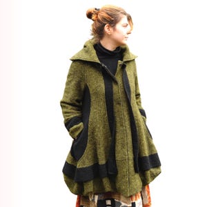 May include: Olive green and black wool coat with a unique design. The coat features a high collar, black stripes, and large pockets. The coat is knee-length and has a flared skirt. The coat is made of a textured wool fabric.