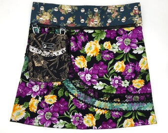 Puede incluir: Una falda floral negra y morada con cremallera y un pequeño bolsillo negro. La falda tiene una capa de encaje en la parte inferior.