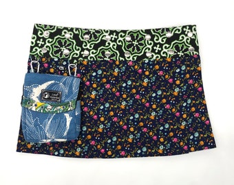 May include: A blue and white floral print mini skirt with a black and green patterned waistband. The skirt has two small pockets on the front, one of which has a small blue and white patterned pouch with the text "ZARA Amsterdam" on it.